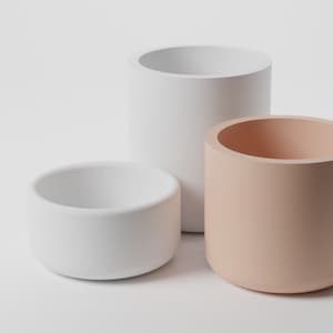 以下が含まれることがあります： 円筒形のプランターが3つ、1つは白、1つは白、1つは薄いピーチ色です。