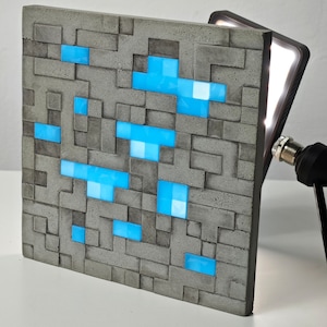 May include: A gray concrete block with a pixelated design of a blue figure. The block is illuminated by a light source.