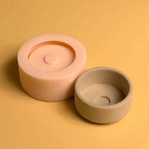 May include: Two round silicone molds for making candles or soap. The larger mold is peach colored and the smaller mold is brown.