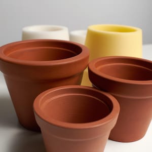 Könnte beinhalten: Vier Terrakotta-Blumentöpfe in verschiedenen Größen. Der größte Topf ist braun, die nächsten beiden sind hellbraun und der kleinste Topf ist hellgelb.