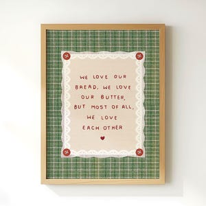 May include: A framed print with a green plaid background and a cream-coloured centre. The centre has a quote that reads, "We love our bread, we love our butter, but most of all, we love each other."