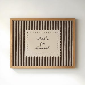 Może przedstawiać: Oprawiona grafika ścienna z jasną drewnianą ramą. Grafika przedstawia beżowe tło z pionowymi brązowymi paskami. Centralny beżowy kwadrat zawiera napis "What's for dinner?" w stylu odręcznym.
