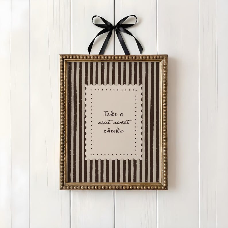 Funny bathroom wall art featuring brown vertical stripes and “Take a Seat Sweet Cheeks” typography inside scalloped vintage cream frame