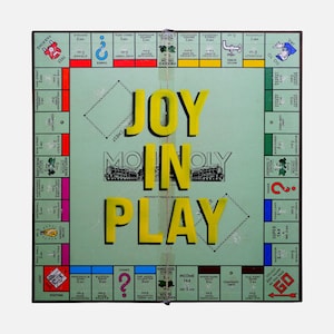 Puede incluir: Un juego de mesa Monopoly vintage con una superficie de juego verde. Las palabras "JOY IN PLAY" se muestran en letras amarillas. El tablero presenta espacios de propiedad, ferrocarriles y áreas de Suerte y Caja de Comunidad.