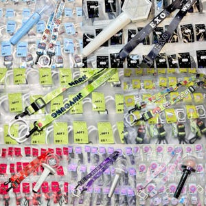 Può includere: Assortimento di lacci colorati con vari nomi di band e loghi, tra cui GOT7, EXO e WEA. I lacci sono esposti su uno sfondo bianco con imballaggio in plastica trasparente.