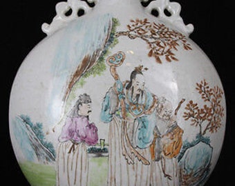 Op de afbeelding: Een witte porseleinen vaas met een rond lichaam en twee handvatten. De vaas is versierd met een scène van drie figuren in een landschap. De figuren zijn geschilderd in tinten blauw, groen en rood. De vaas heeft een witte glazuur en is versierd met een rode inscriptie op de hals.