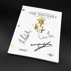 May include: A white screenplay titled The Odyssey, a film by Christopher Nolan, featuring a gold Spartan helmet graphic, three black ink signatures, and the Syncopy and Universal logos. The document is bound with three gold-colored metal fasteners.