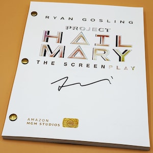 May include: A white screenplay titled Project Hail Mary featuring the name Ryan Gosling at the top and Amazon MGM Studios at the bottom. The cover includes a black ink signature, metallic gold binding fasteners, and a gold holographic authentication sticker.
