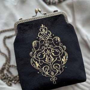 Puede incluir: Un bolso de mano de terciopelo negro con una cadena dorada y un diseño floral bordado en oro.
