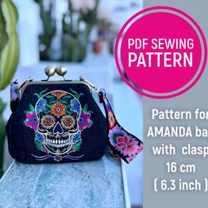 Könnte beinhalten: Eine schwarze Tasche mit Verschluss, mit einem gestickten Sugar-Skull-Design mit bunten floralen Akzenten. Die Tasche ist 16 cm breit. Der Text "PDF SEWING PATTERN" und "Pattern for AMANDA bag with clasp" ist ebenfalls enthalten.