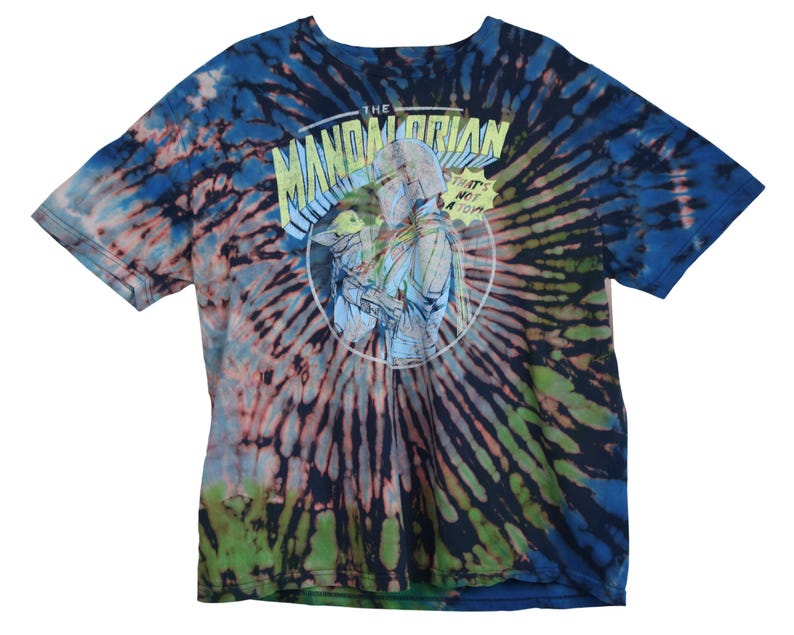 May include: Tie-dye t-shirt with a graphic from The Mandalorian. The shirt features a spiral pattern in shades of blue, green, and pink. The graphic is a circular design with the text "The Mandalorian" and "That's not a toy".