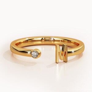 May include: A gold ring with a single diamond and the letter "M" on the side.
