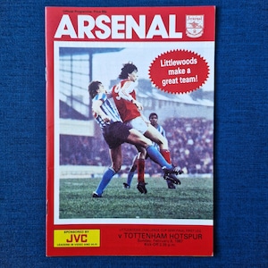 May include: An Arsenal football programme from 8 February 1987, featuring a photo of two players in action. The programme is sponsored by JVC and advertises Littlewoods, a department store chain.