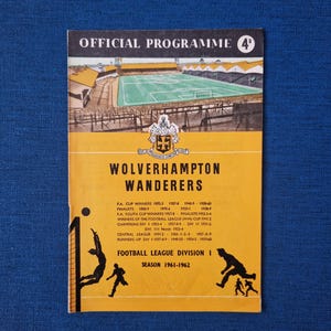 May include: A yellow and black programme for a Wolverhampton Wanderers football match. The programme features the team's crest and the text "OFFICIAL PROGRAMME 4°" at the top. The programme also includes the text "WOLVERHAMPTON WANDERERS" and lists the team's achievements, including FA Cup wins, youth cup wins, and league championships. The programme is for the 1961-1962 season of the Football League Division I.