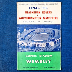 May include: A vintage football programme for the 1960 Football Association Challenge Cup Final Tie. The programme features Blackburn Rovers versus Wolverhampton Wanderers. The cover has a stadium illustration and text that reads "Empire Stadium Wembley".