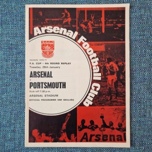 May include: A black and white programme for an Arsenal Football Club match against Portsmouth. The programme is for the 4th round replay of the F.A. Cup on Tuesday, 26th January, 1971. The programme features a photo of Arsenal players in action and the text "Arsenal Football Club".