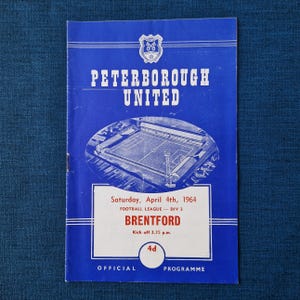 May include: A vintage blue and white official programme for a football match between Peterborough United and Brentford, dated April 4th, 1964. The cover features the team names, a stadium illustration, and the price of 4d.