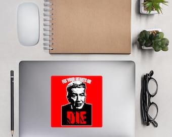 May include: A square sticker with a red background features a black and white portrait of a man. The text "FIX YOUR HEARTS OR DIE" is printed in white and red. The sticker is placed on a gray laptop.