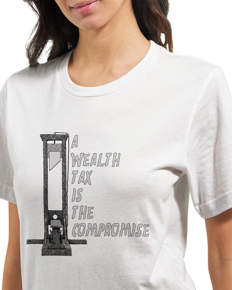 May include: White t-shirt featuring a black and white illustration of a guillotine. The text on the shirt reads "A Wealth Tax Is The Compromise". The design is centered on the front of the shirt.