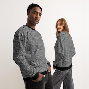 Könnte beinhalten: Zwei Personen tragen passende graue Sweatshirts mit einem detaillierten, symmetrischen Muster. Die Sweatshirts haben schwarze Abschlüsse an Kragen, Manschetten und Saum. Der Hintergrund ist schlicht weiß.
