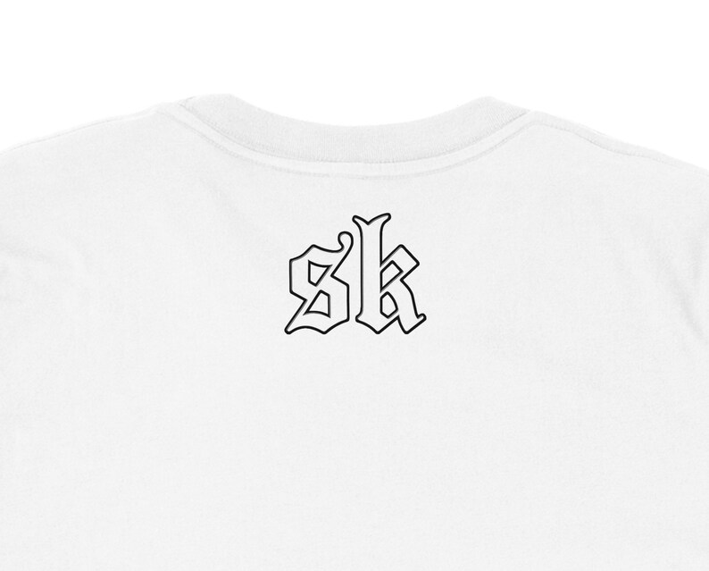 May include: White crew neck t-shirt with a black gothic-style "SK" logo on the back. The logo is outlined in black, creating a bold contrast against the white fabric. The shirt's neckline is visible.