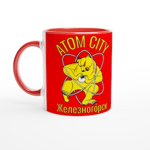 May include: A white ceramic mug with a black handle and the text "But First, Coffee" in a bold, black font. The mug is set against a blurred background, suggesting a cozy setting. The mug appears to be approximately 4 inches tall.