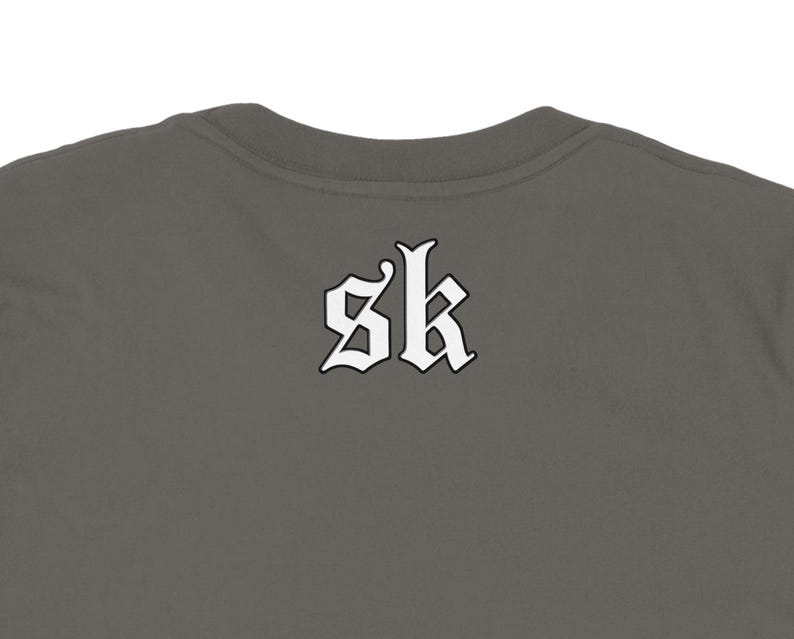 May include: A dark gray t-shirt with the white letters "sk" in a gothic font on the back. The shirt has a crew neck and is made of a soft material.