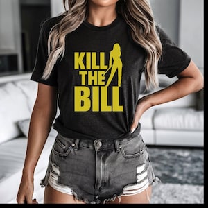 May include: Dark gray t-shirt with the text "KILL THE BILL" in yellow, along with a silhouette of a person holding a weapon. The shirt is a crew neck style.