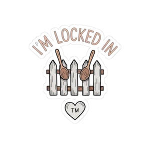 May include: A sticker with the text "I'M LOCKED IN" in a light brown color. The design features two wooden spoons over a white picket fence. A heart with "TM" inside is at the bottom.
