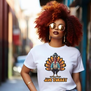 Puede incluir: Camiseta blanca con un pavo de dibujos animados que lleva gafas de sol y un sombrero. El pavo lleva una camisa azul y pantalones marrones. El texto "Jive Turkey" está impreso debajo del pavo.