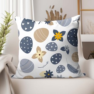 May include: A white throw pillow with a blue and yellow Easter egg pattern. The pillow features a variety of blue and yellow eggs with white polka dots, hearts, and stripes. The eggs are surrounded by yellow flowers with blue centers.