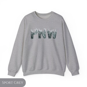 May include: A heather grey sweatshirt with the text "PNW" in a forest green font. The letters are made up of a pattern of evergreen trees.