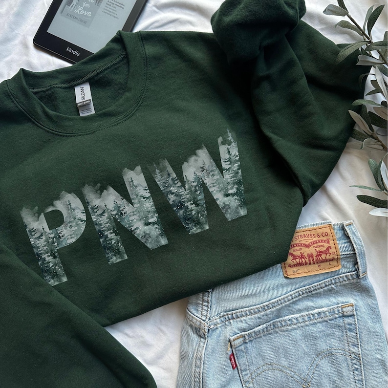 May include: A dark green sweatshirt with a white graphic print of the letters "PNW" with a snowy forest scene inside each letter.
