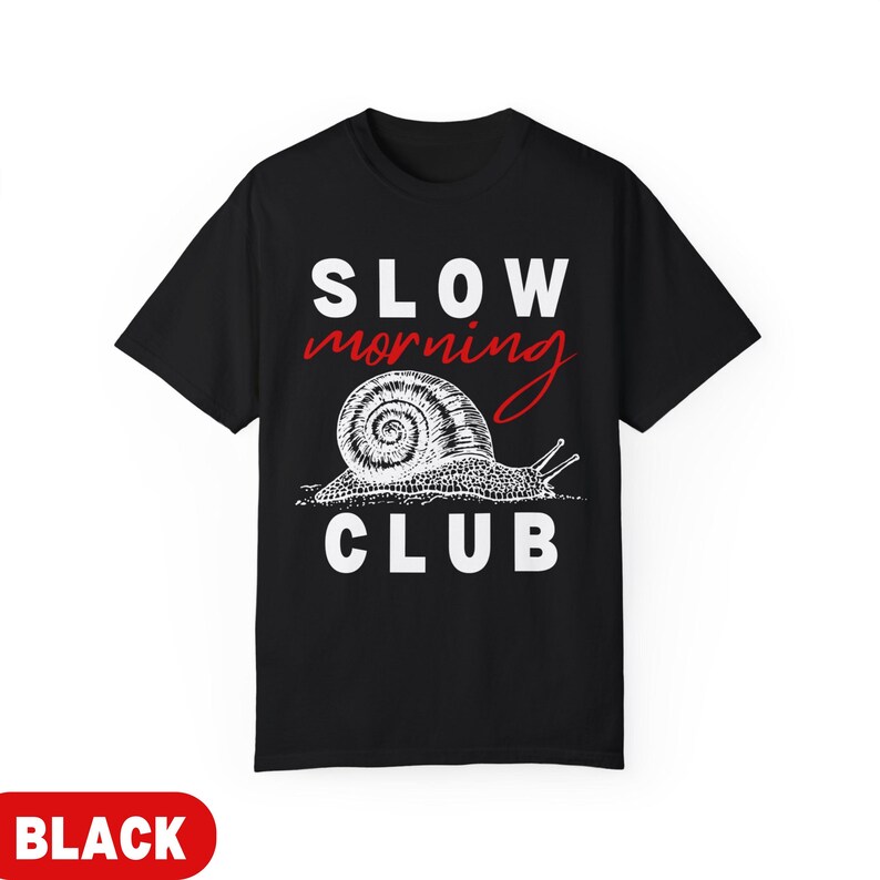 K&ouml;nnte beinhalten: Schwarzes T-Shirt mit dem Schriftzug "SLOW MORNING CLUB" in Wei&szlig; und Rot. Unter dem Text befindet sich eine detaillierte Illustration einer Schnecke. Das T-Shirt hat einen Rundhalsausschnitt.