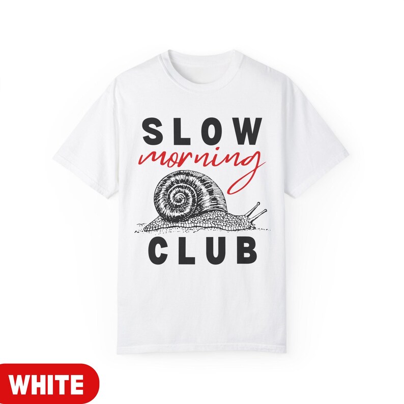 K&ouml;nnte beinhalten: Wei&szlig;es T-Shirt mit dem Text "SLOW MORNING CLUB" in Schwarz und Rot. Darunter befindet sich eine detaillierte Illustration einer Schnecke. Ein l&auml;ssiges Kleidungsst&uuml;ck f&uuml;r den Alltag.