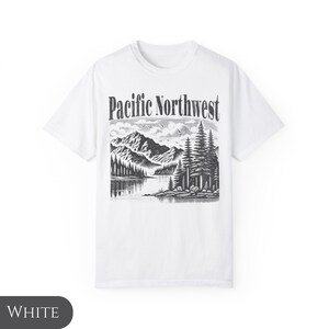 Może przedstawiać: Biała koszulka z czarno-białym nadrukiem graficznym przedstawiającym g&oacute;rską scenerię i tekst "Pacific Northwest".