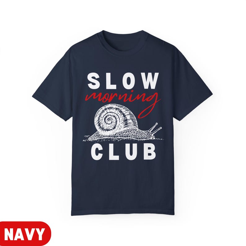 K&ouml;nnte beinhalten: Marineblaues T-Shirt mit den W&ouml;rtern "SLOW" und "CLUB" in wei&szlig;en Blockbuchstaben. Das Wort "morning" ist in roter Schreibschrift. Eine detaillierte Illustration einer Schnecke befindet sich in der Mitte. Das Wort "NAVY" steht in einem roten Rechteck unten.