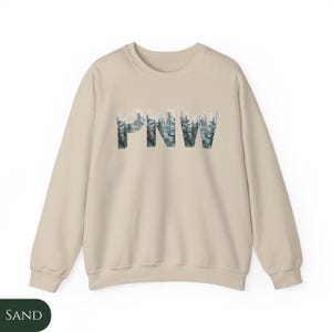 May include: A sand colored sweatshirt with a graphic print of the letters "PNW" made up of a forest scene.