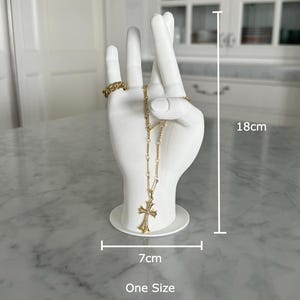 K&ouml;nnte beinhalten: Wei&szlig;er Keramik-Hand-Schmuckhalter mit einer goldenen Kettenkette und einem Kreuzanh&auml;nger. Die Hand ist 18 cm hoch und 7 cm breit. Einheitsgr&ouml;&szlig;e.