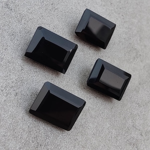 May include: Four black rectangular gemstones with a polished finish. The gemstones are arranged in a staggered pattern on a gray surface.
