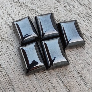 May include: Five black, rectangular, polished gemstones arranged in a staggered pattern. The gemstones are smooth and reflective.
