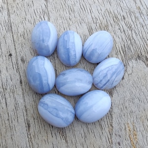 May include: Eight smooth, oval-shaped blue agate stones with white and gray banding. The stones are arranged in a circle on a light wood surface.