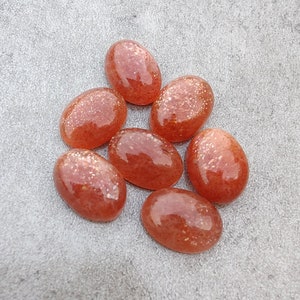 May include: Seven oval-shaped sunstone cabochons in shades of orange and red with a shimmery, glittery finish.