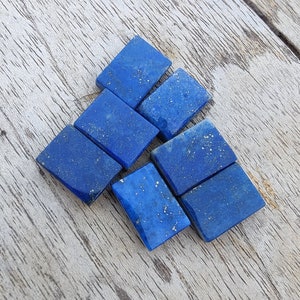 Puede incluir: Un grupo de seis pequeñas piedras rectangulares de lapislázuli. Las piedras son de color azul intenso con motas doradas.