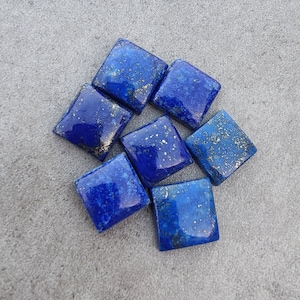May include: Seven square-shaped lapis lazuli gemstones with gold flecks. The stones are arranged in a cluster on a gray surface.