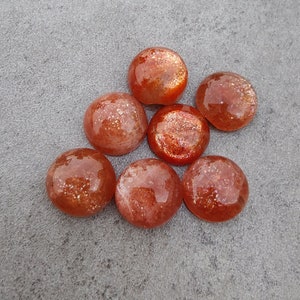 Puede incluir: Siete cabujones de piedra de sol naranja lisos y redondos con un acabado brillante e iridiscente.
