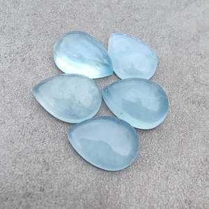 May include: Five teardrop-shaped aquamarine gemstones, each with a smooth, polished surface and a light blue colour.