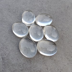 May include: Eight clear glass oval-shaped stones, arranged in a circular pattern on a gray surface.