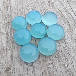 Pu&ograve; includere: Otto pietre preziose rotonde, lisce e di colore azzurro chiaro. Le pietre preziose sono disposte in cerchio su una superficie di legno marrone chiaro.