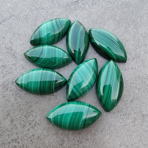 Puede incluir: Una colección de ocho cabujones de malaquita verde, cada uno con un patrón único de líneas verdes en espiral. Los cabujones tienen forma de óvalos alargados y un acabado liso y pulido.